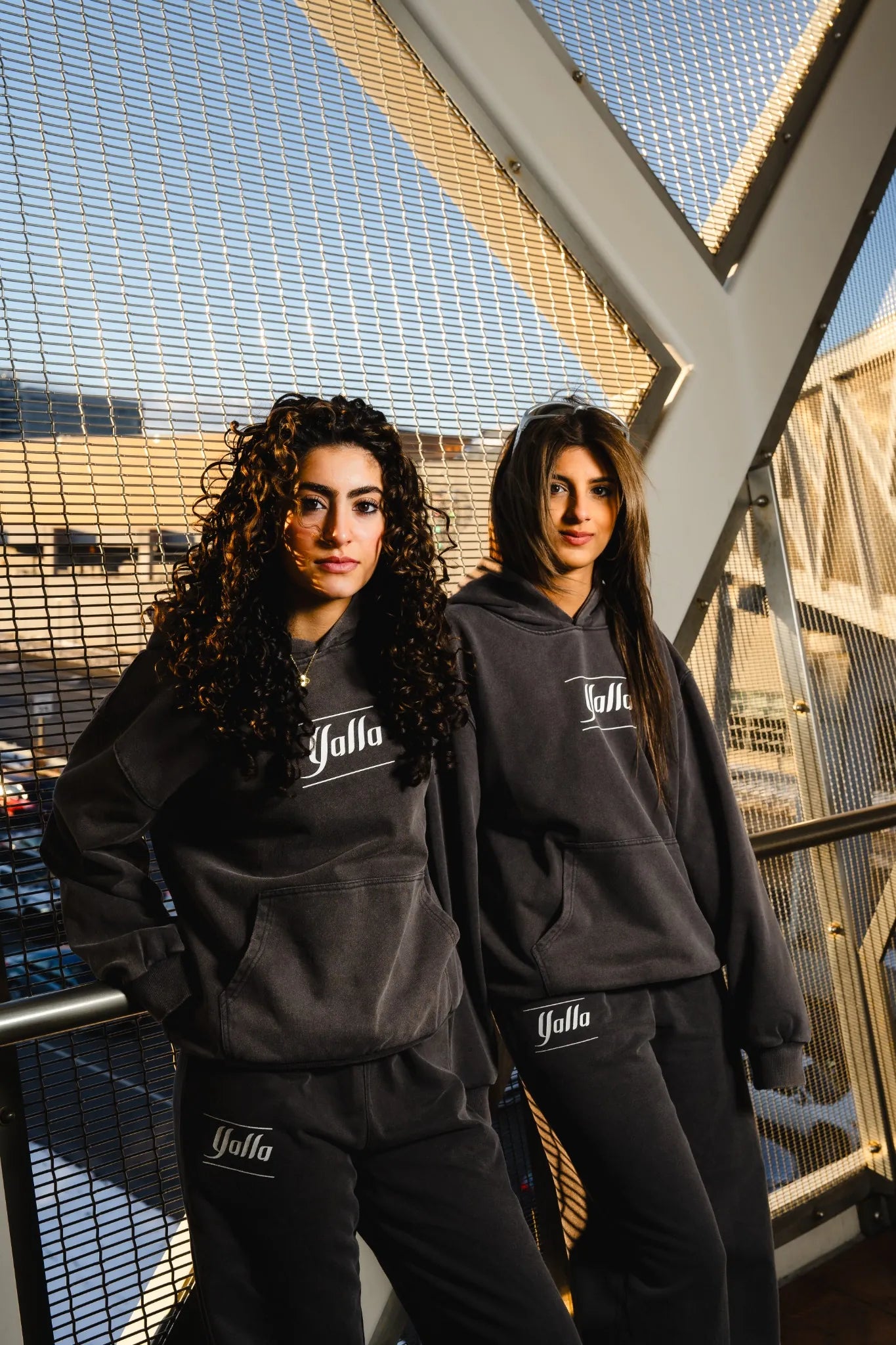 Two female models wearing modest Timeless Arab Tracksuits by Yalla Apparel, designed for comfort, Arab identity, and minimalist street style. The perfect dark grey tracksuit.