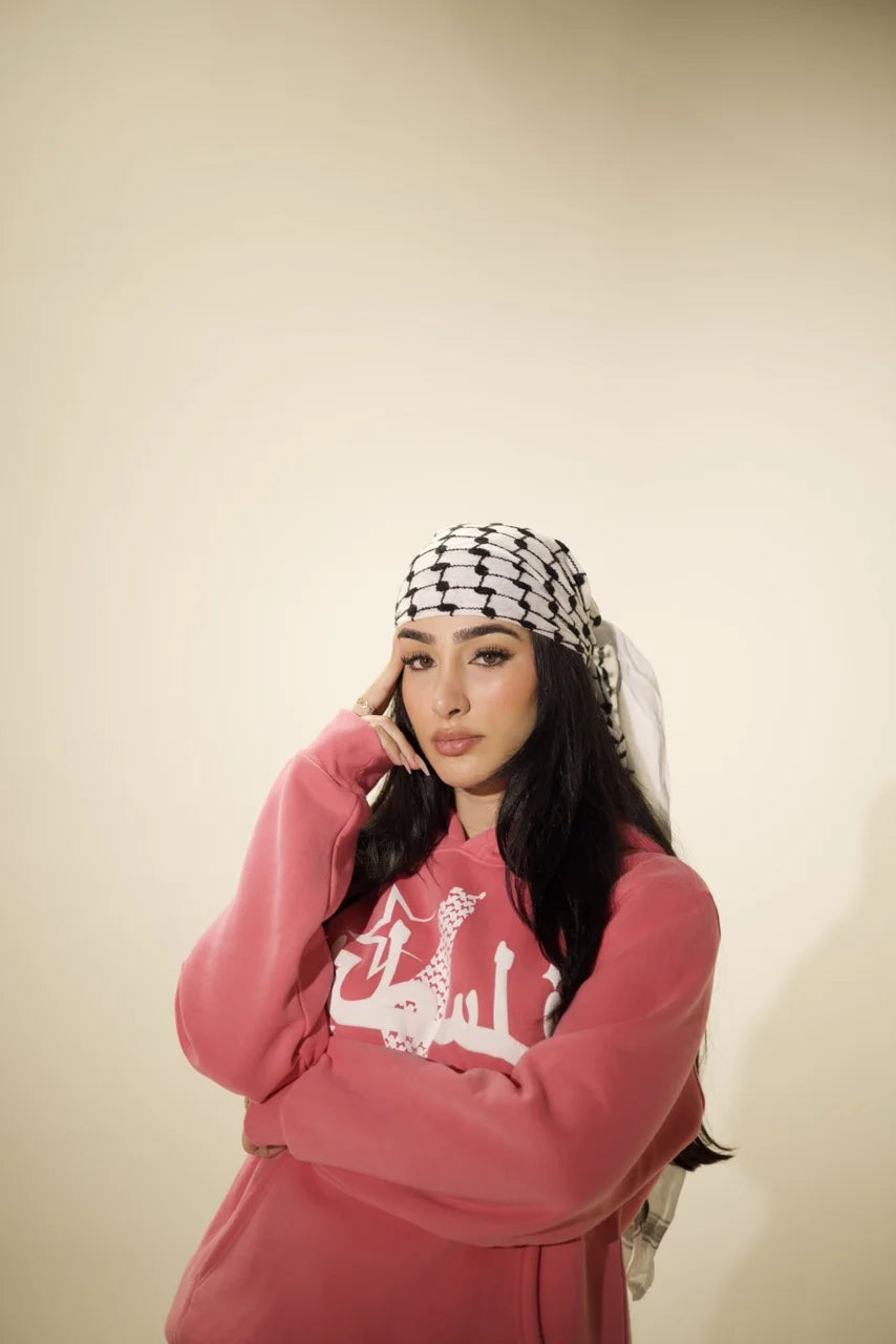 Famous influencer Adolla wearing Peace Pink Hoodie, a modern Palestinian streetwear piece with Kufiya-inspired design and Arabic typography."