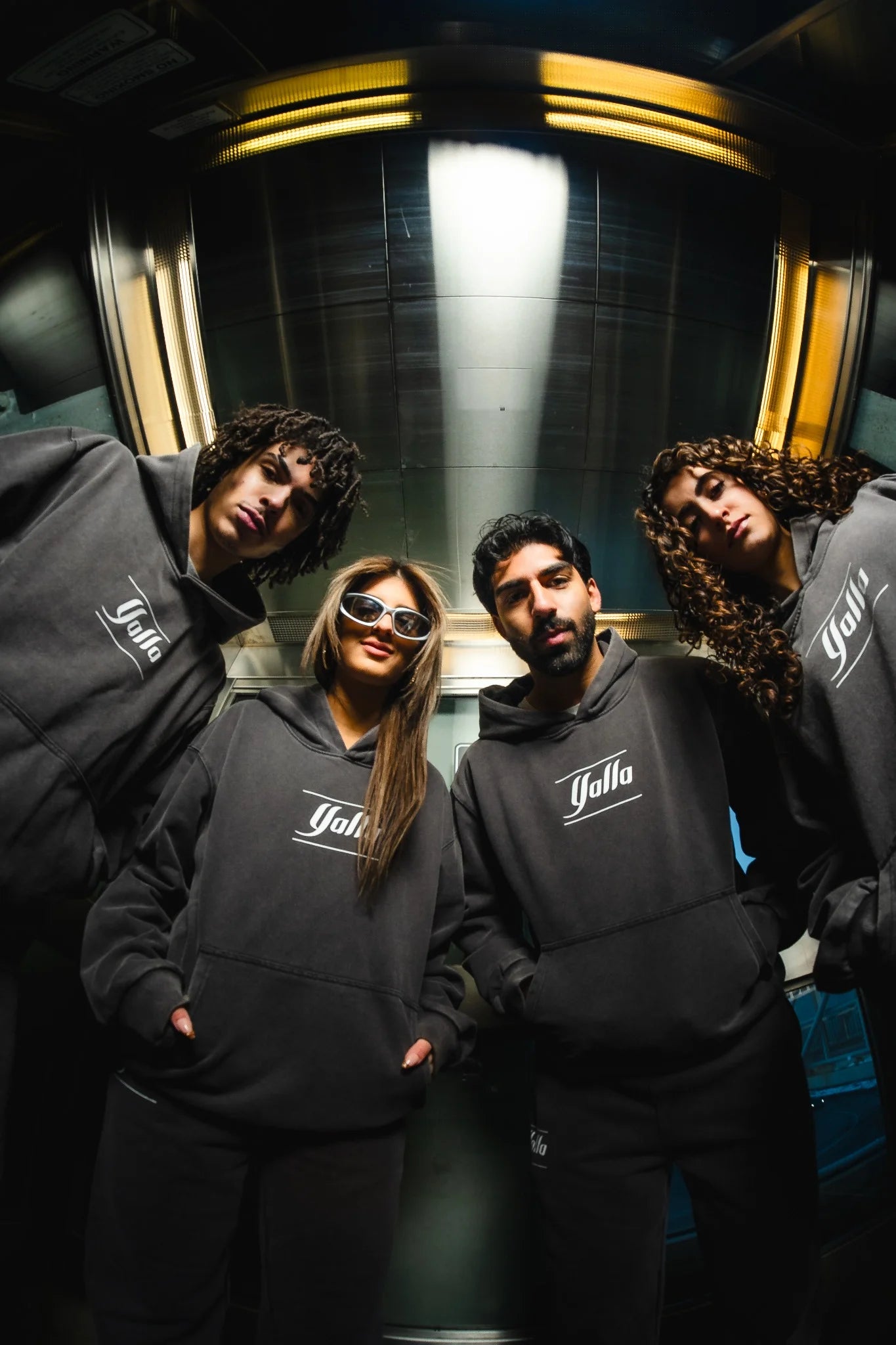 Four models wearing the Yalla Tracksuit in an urban setting. Premium Arab streetwear with a relaxed, modern fit. Stylish black hoodie and sweatpants set featuring the Yalla logo. On the back there is the name of all the Arab Countries to show inclusivity.