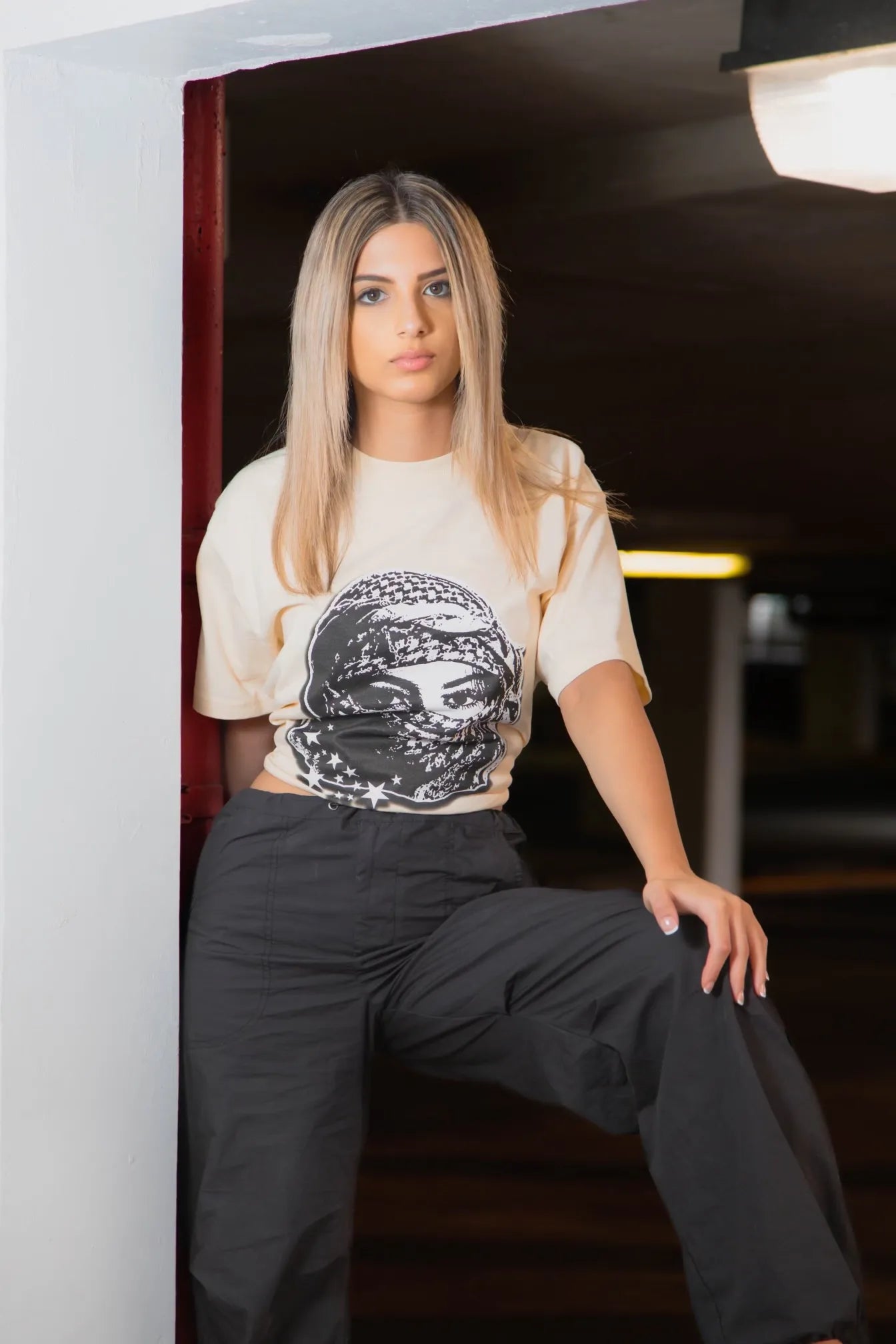 Women model wearing Arab streetwear, showcasing the Sand Kufiya Graphic Tee with cultural design elements.
